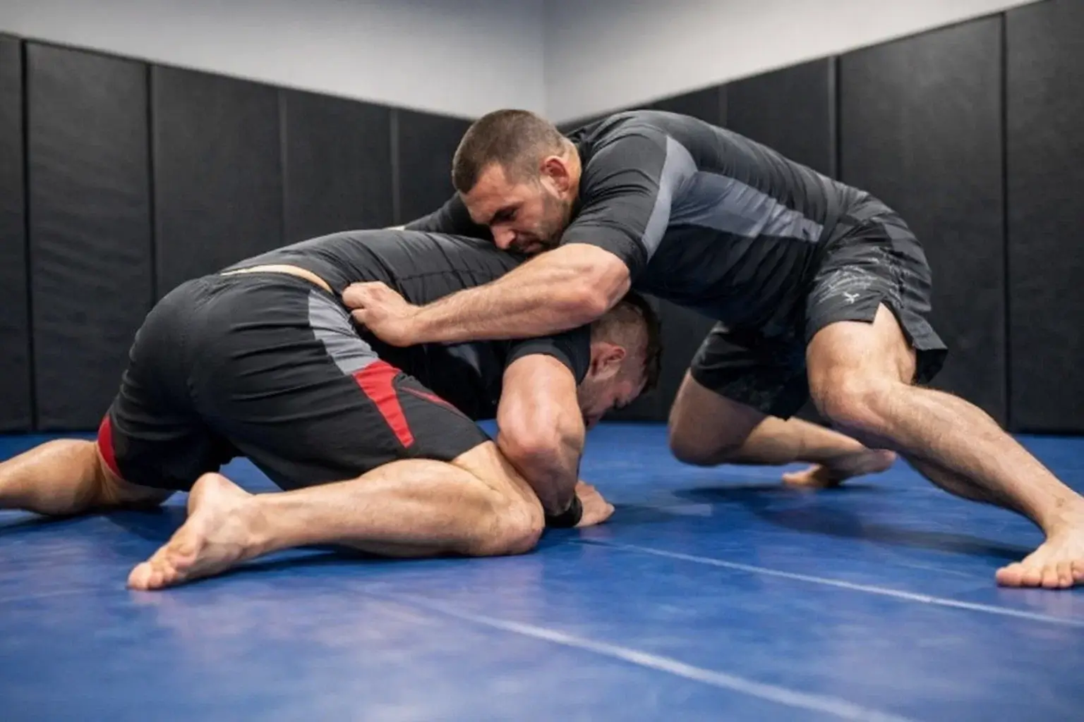 Two fighters practicing wrestling takedowns on training mat